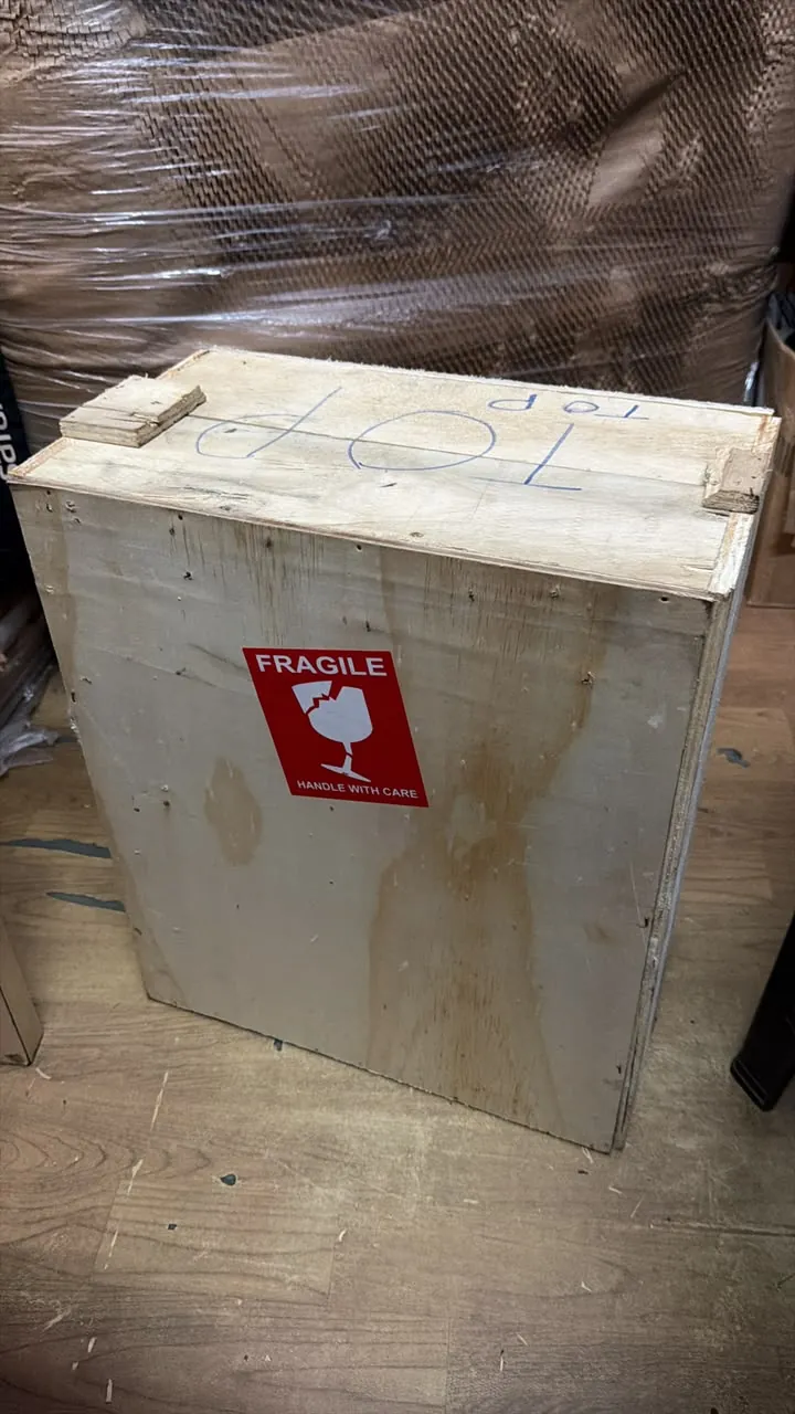 Plywood crate marked TOP with a red Fragile handle-with-care sticker